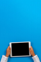 Kid hand holding white digital tablet computer on light blue background. Top view