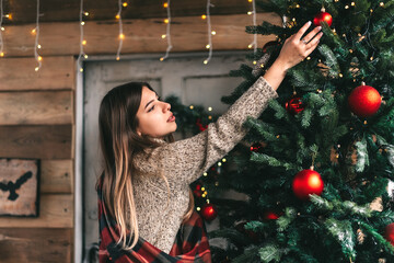 Young caucasian woman in a plaid decorates a christmas tree on the veranda of a wooden house.