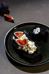 Sandwich with Ricotta, blue cheese and fresh Figs on plate on dark concrete background. Simple healthy breakfast. Smørrebrød. Very black bread