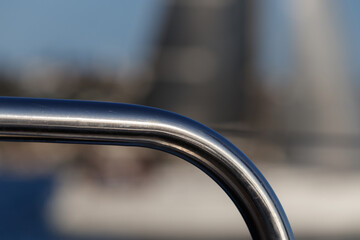 Close up of a metal rod on a sailboat,  with a boat, ocean and land in with selective focus background