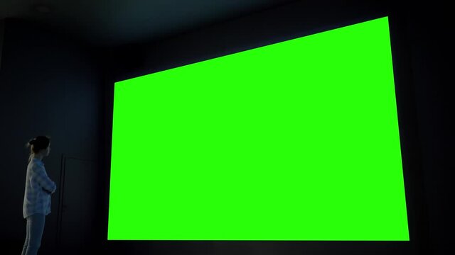 Green screen, technology, chroma key, futuristic, template, mock up, entertainment concept. Woman looking at large wall blank interactive green display at science exhibition, museum or cinema