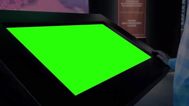 Green screen, futuristic, mockup, science, copyspace, template, chroma key, technology concept. Woman looking at blank green display of interactive kiosk in dark room of exhibition or museum