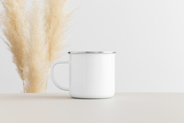 Enamel white mug mockup on a beige table with pampas decoration.