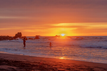 Sunset on the beach, with people playing in the sea