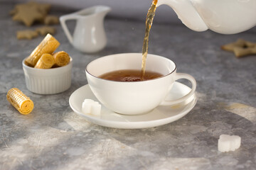 Tea from the teapot is poured into a white mug. A stream of tea pours into the Cup with a splash