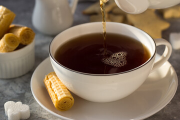 Tea from the teapot is poured into a white mug. A stream of tea pours into the Cup with a splash