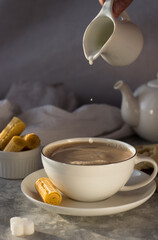 Milk from the milk jug drips into a white mug of tea. the water in the Cup ripples with drops