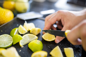 Male hands slicing lemons and limes on a black tray
