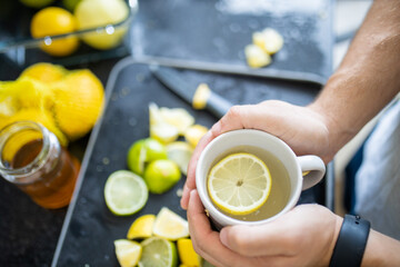 Male hands holding a cup of lemon tea above lime slices