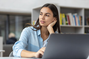 Beautiful young woman working using laptop while sitting at home office. Remote work or learning concept