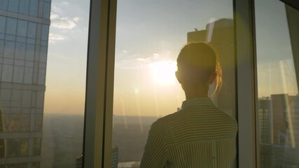 Back view of woman silhouette looking at cityscape through window of skyscraper. Summer time, sunset, sun lens flare. Success, business, opportunity, sightseeing, corporate, discover, future concept
