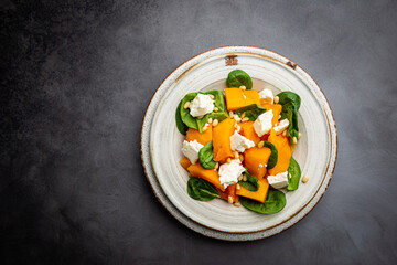 Salad with roasted pumpkin, cheese, spinach, Pine nuts and seasonings on dark background, top view