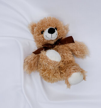 A light brown Teddy bear lies on a white knitted fabric.