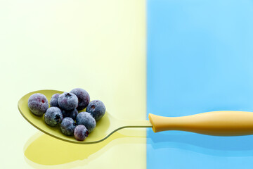 Yellow spoon with frozen blueberries on a two-tone yellow-blue background. Copy space.