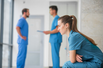 Young female doctor feeling upset while her colleagues talking