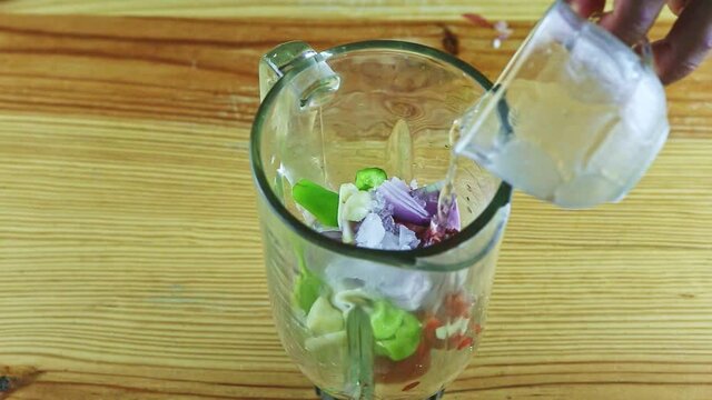 top view closeup on mand hands pours clear water from glass cup into blender chalice
