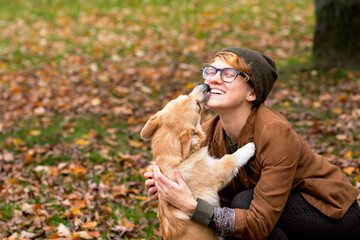 Happy woman hugs and kisses her dog, corgi breed. In the park outdoors