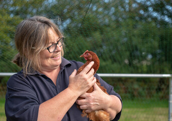 Happy mature woman holding a chicken outdoors 
