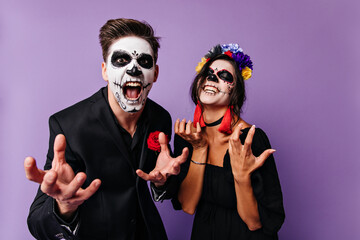 Angry boy and girl in masks of skull emotionally pose, wanting to show their greatness. Portrait of dark-haired mexican couple