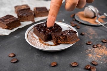 Cocoa brownies pouring with melted dark chocolate cut out to square pieces on a white plate. Black...