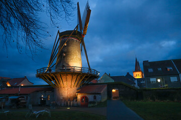 Night city view and windmill after rain in the street of Duisburg, with lantern switched on in...