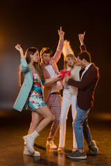 full length of multicultural friends toasting plastic cups and rejoicing during party on black