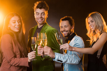  multicultural friends holding glasses of champagne and clinking on black