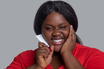Young dark-skinned woman in red clothes holding a tube with face foundation
