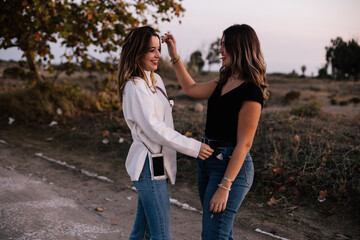 Fototapeta premium Lesbian women couple smiling while showing love. They are dressed casually. One girl touches her hair and the other girl her waist