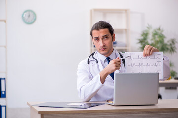 Young male doctor looking electrocardiogram in the clinic