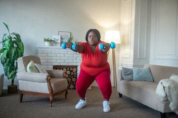 Plus size african american woman doing squats with dumbbells