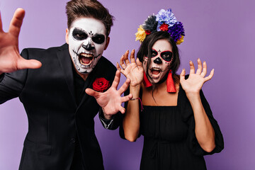 Closeup portrait on Halloween of man and woman posing with frightening faces. Couple in black clothes with red details screaming