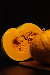 Vertical photo of half a pumpkin with orange flesh. Second part on the right. The background is black, with a wooden Board at the bottom. Transparent drops of juice are visible on the cut.