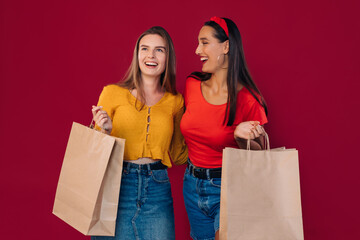 cheerful girls smiling and talking, holding a bag after going to the store, posing against a green background