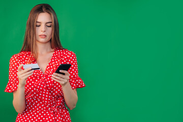 Image of attentive serious attractive young female holding her smartphone and credit card, doing shopping online, using modern technologies, wearing casual clothes. People and technology concept.