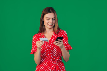 Image of a beautiful happy young girl posing isolated on a wall background holding a credit card using a mobile phone while shopping on the internet.