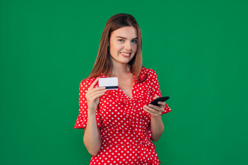 Smiling girl holding a smartphone and a credit card. girl in casual clothes on a green background. The concept of emotions and pleasant feelings, shopping.
