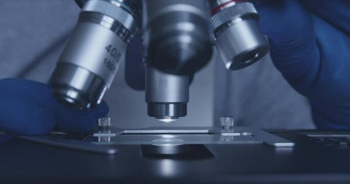 Close-up shot of sample slide and microscope with metal lens at laboratory.