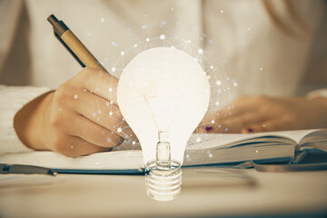 Bulb hologram over hands taking notes background. Concept of idea. Double exposure