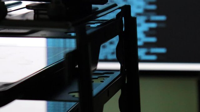 blue computer software code moving on a black monitor reflect on glass. Abstract computer hacking in process with rack server base, dynamic text running and flowing on pc screen