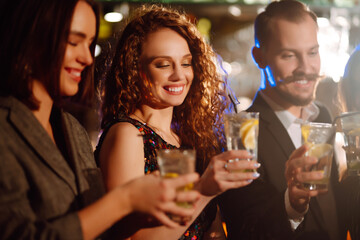 Happy friends cheering and drinking cocktails enjoying party in the club.  Group of young people  clinking by glases with cocktails in the bar. Youth, lifestyle and nightlife concept.