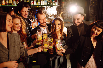 Happy friends cheering and drinking cocktails enjoying party in the club.  Group of young people  clinking by glases with cocktails in the bar. Youth, lifestyle and nightlife concept.
