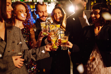 Happy friends cheering and drinking cocktails enjoying party in the club.  Group of young people  clinking by glases with cocktails in the bar. Youth, lifestyle and nightlife concept.