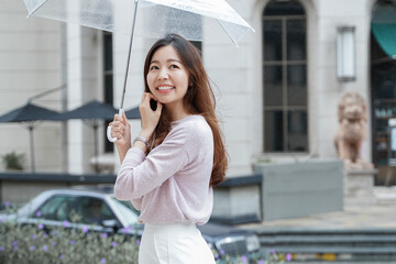 Fototapeta premium Young Asian woman smile and holding a transparent umbrella under the rain in the city