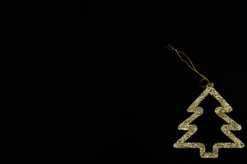 Fototapeta premium Minimalistic golden Christmas tree on a black background. New year simple composition. Merry Christmas and happy New Year greeting card.