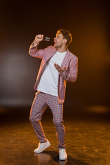 full length of man singing while holding microphone on black, stock image