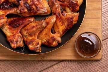 Fried spicy chicken wings with sauce on a pan on a wooden background. The view from the top. Fast food.