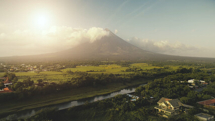 Sun shine over Mayon volcano eruption aerial. River at green grass hillside. Tropic forest at...