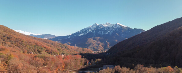 Panorama with colourful autumn forest and beautiful mountains with snow peaks. Sochi, Krasnaya Polyana, Russia.