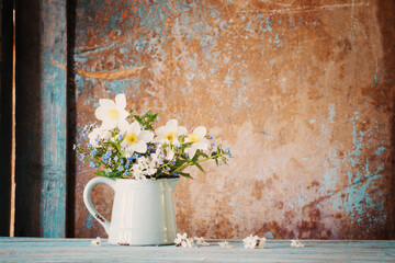 spring flowers in jug on old wooden painted background